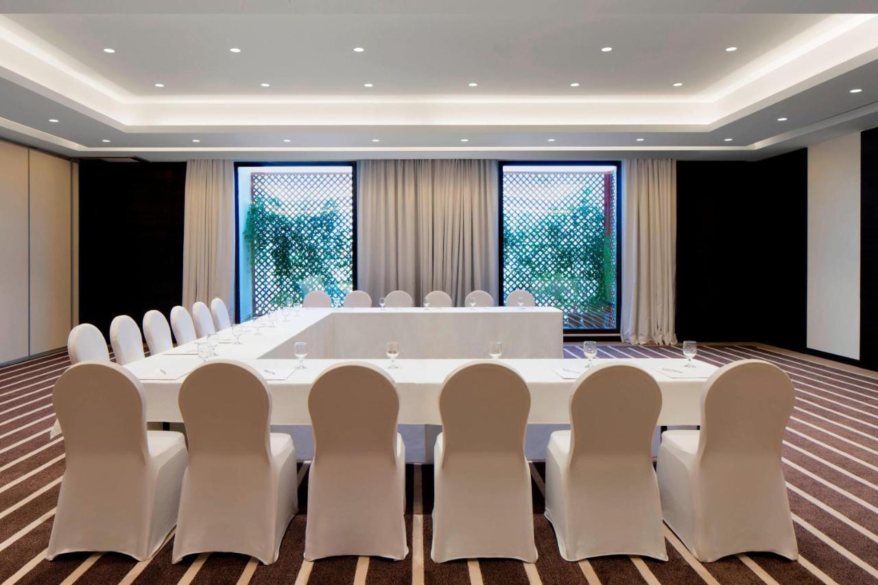 Le Meridien Dubai Hotel & Conference Centre Buitenkant foto The photo shows a modern conference room designed for meetings or gatherings. It features a long rectangular table covered with a white tablecloth, surrounded by white chairs. The room is well-lit with recessed lighting in the ceiling and has large w